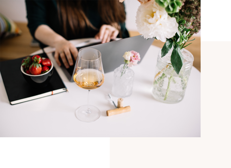 Ragazza che scrive computer con calice di vino e fiori